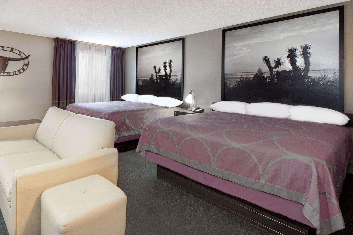 A hotel room with two beds, a sofa, and artwork depicting palm trees and a beach.