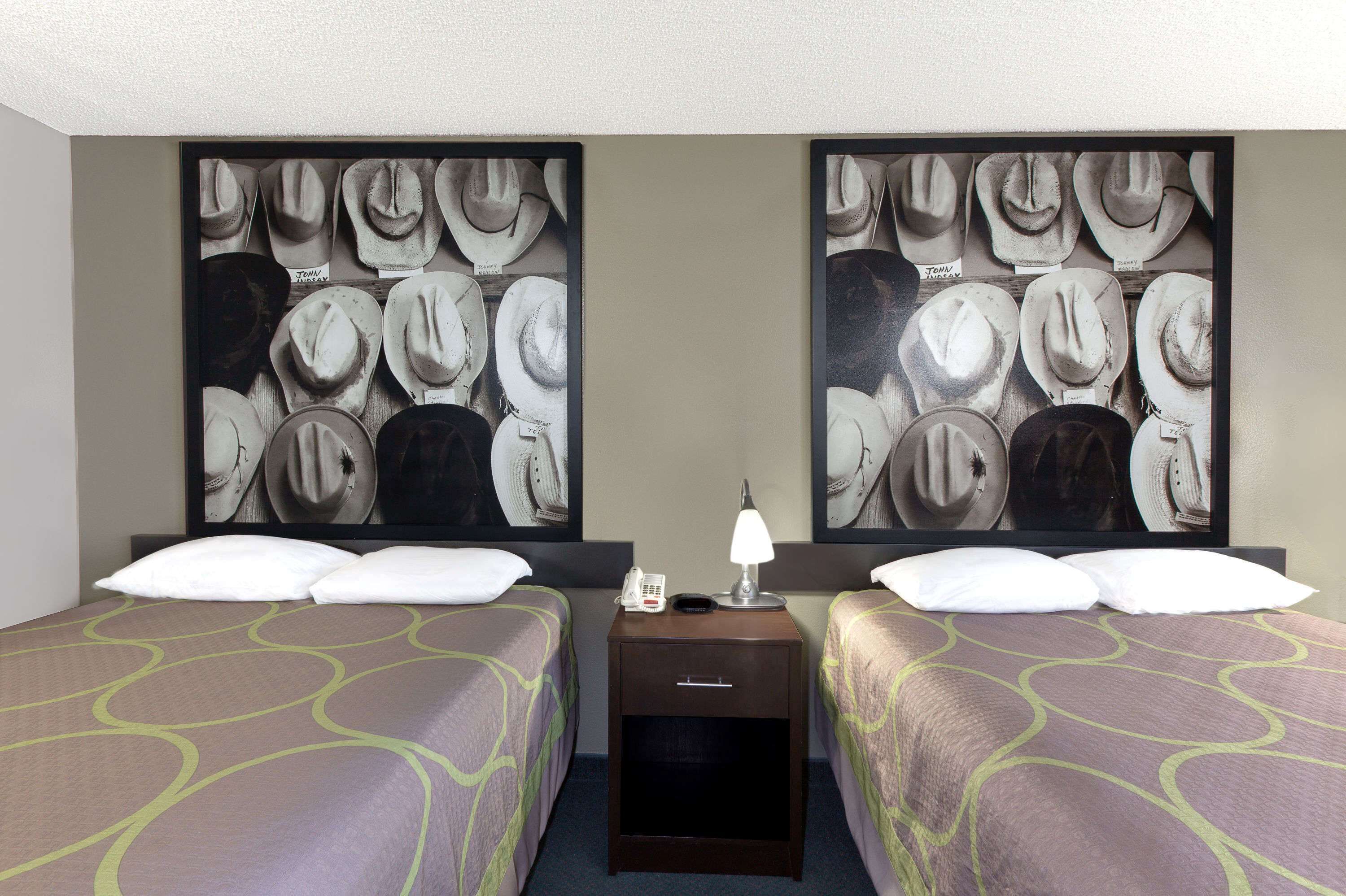Une chambre d’hôtel avec deux lits, une table de chevet avec une lampe et un mur orné d’un grand tableau représentant des chapeaux de cow-boy.