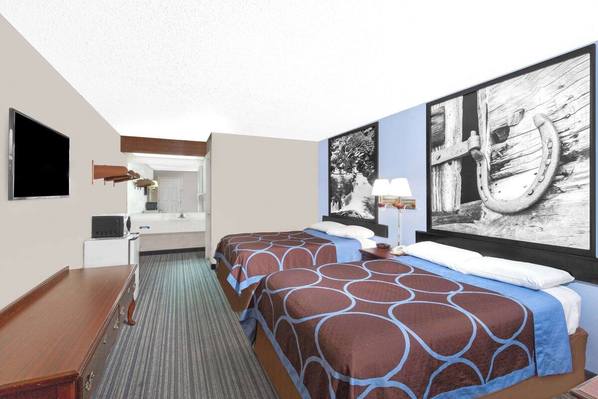 Une chambre d’hôtel avec deux lits, un bureau, un téléviseur à écran plat et des œuvres d’art accrochées aux murs.