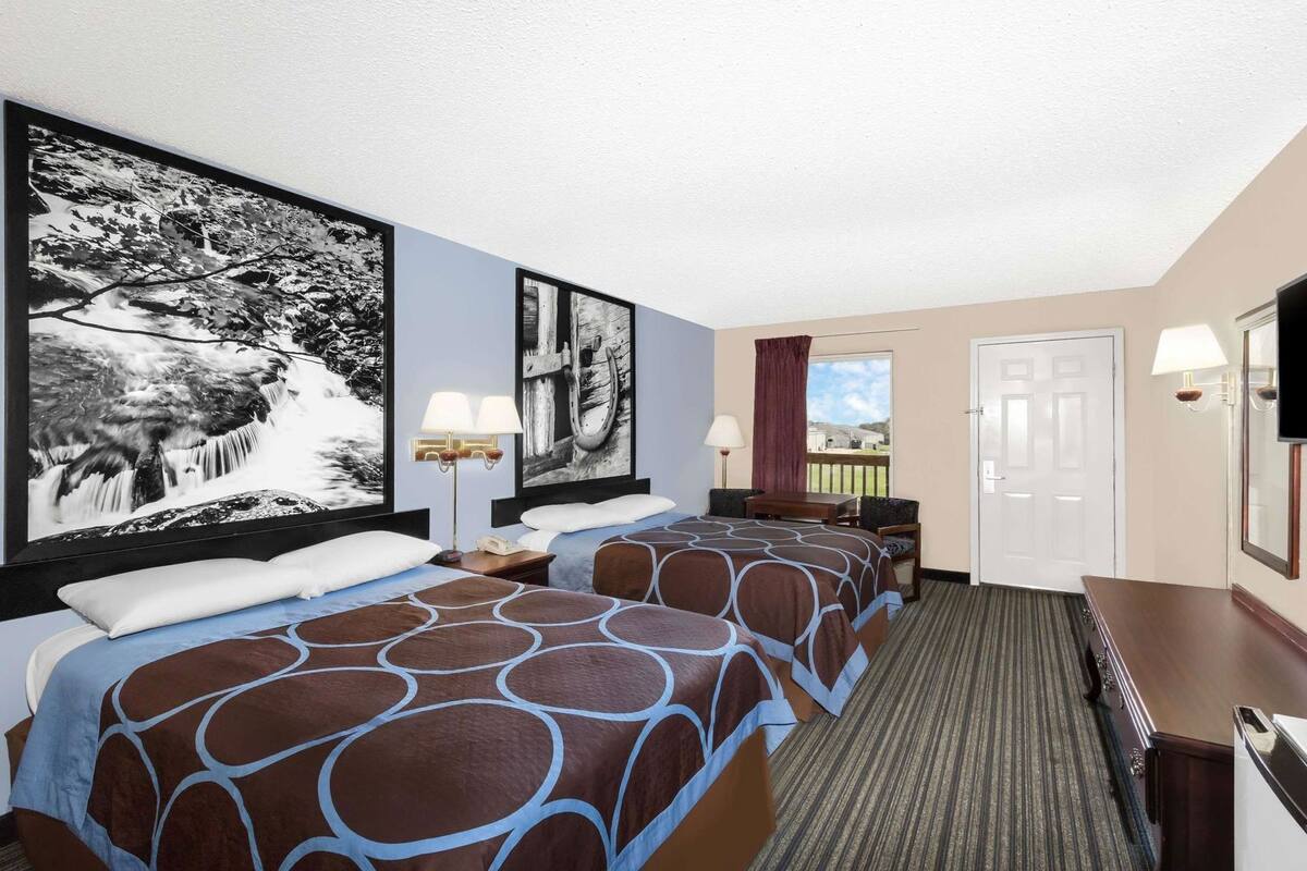 Une chambre d’hôtel avec deux lits, un bureau, une chaise, une télévision et de grandes images encadrées accrochées au mur.