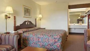 A hotel room with a bed, two bedside lamps, a wooden headboard, a small table, a striped chair, and a mirror above the dresser.