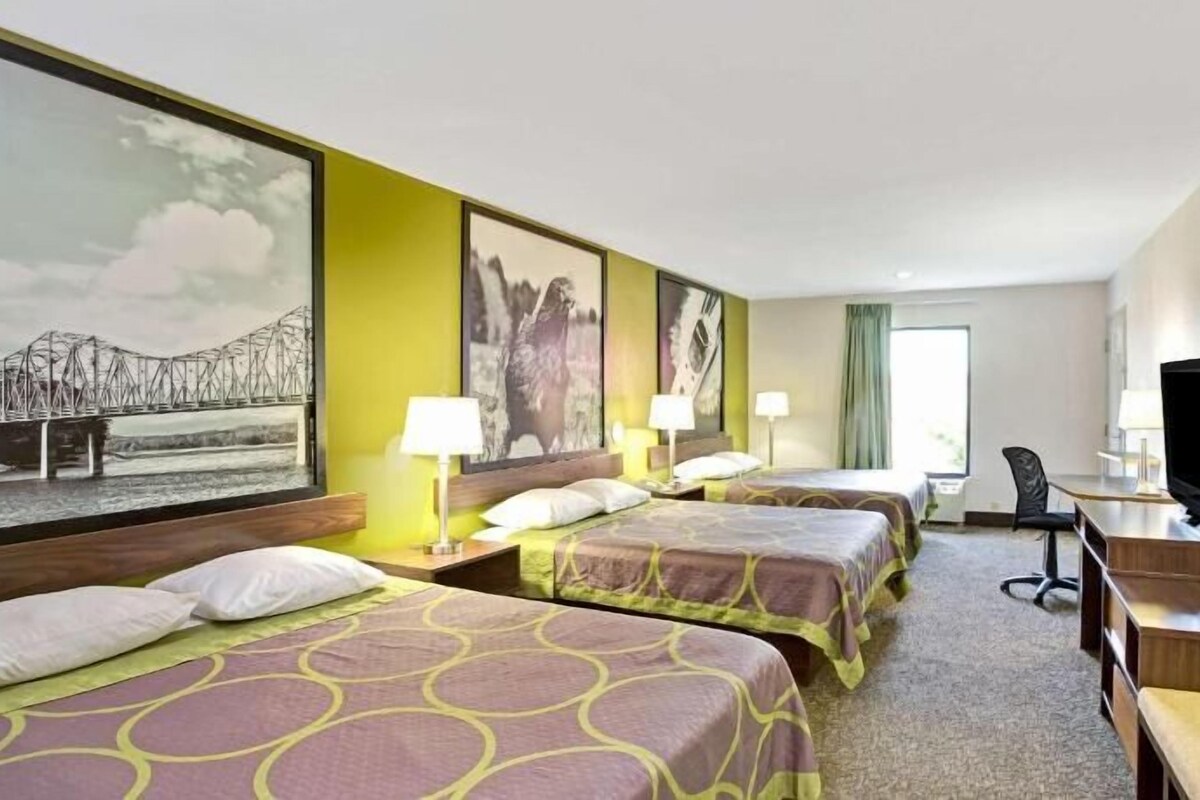 A hotel room with two beds, a desk, a chair, a television, and artwork on the walls.