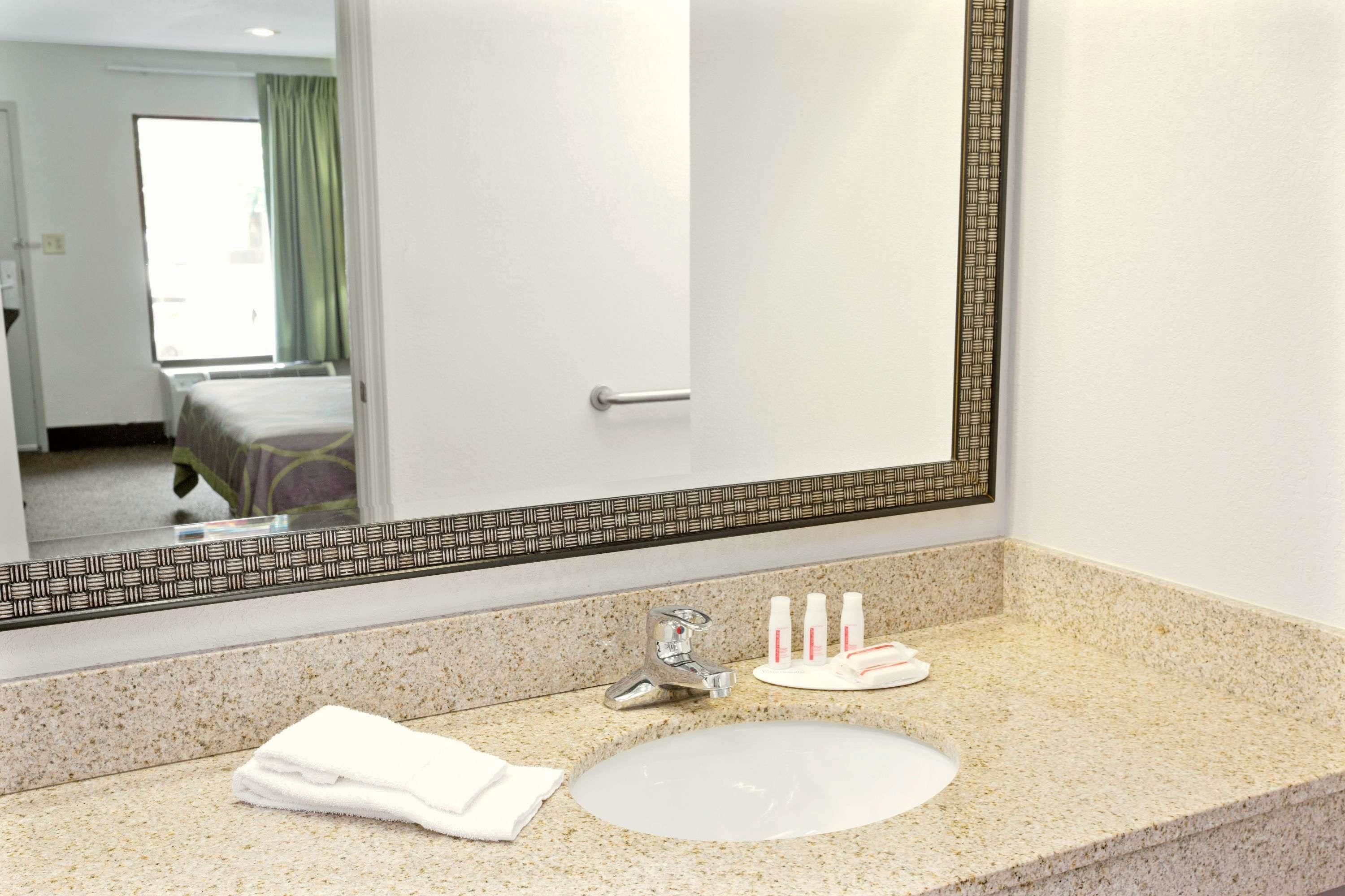 A hotel bathroom with a large mirror, a sink, and toiletries.