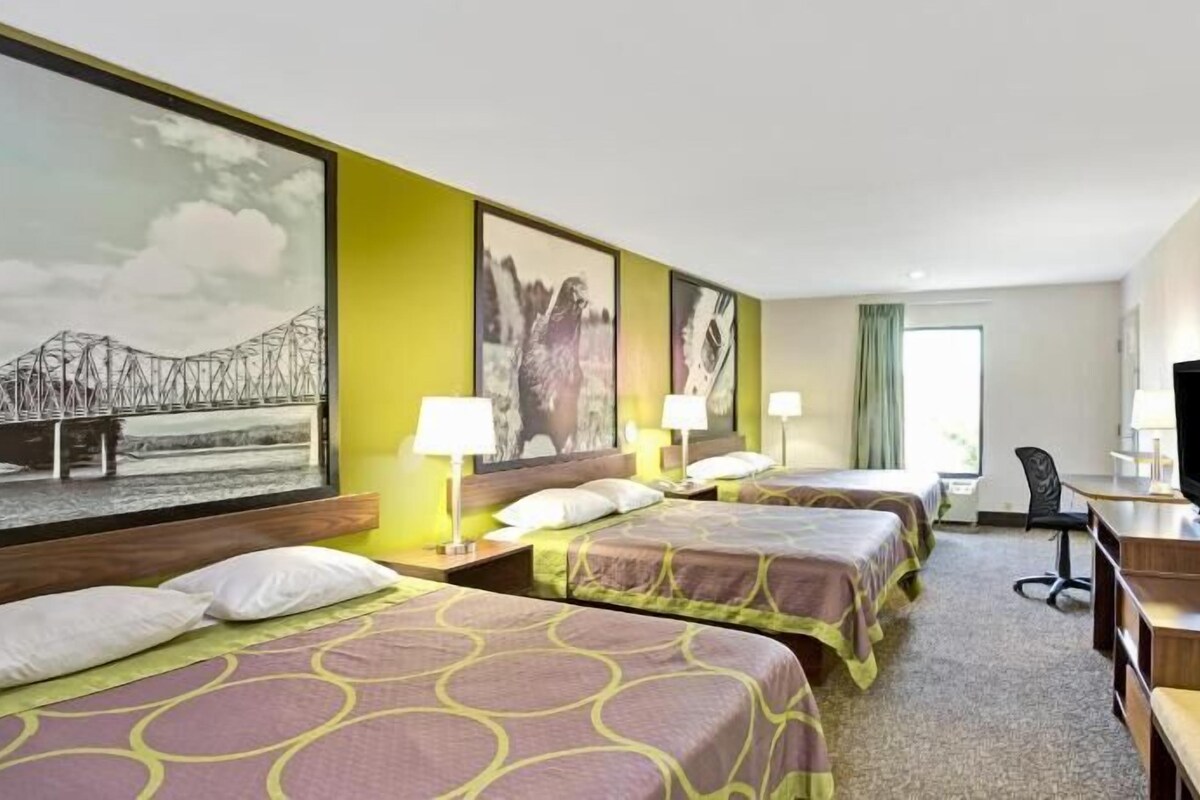 A hotel room with two beds, a desk, a chair, a television, and artwork on the walls.