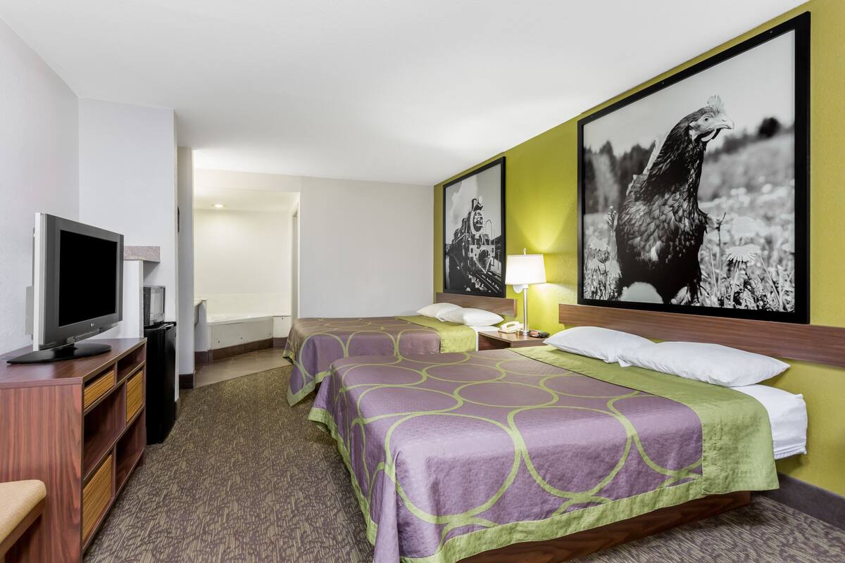 A hotel room with two beds, a TV, a desk, and artwork on the walls.