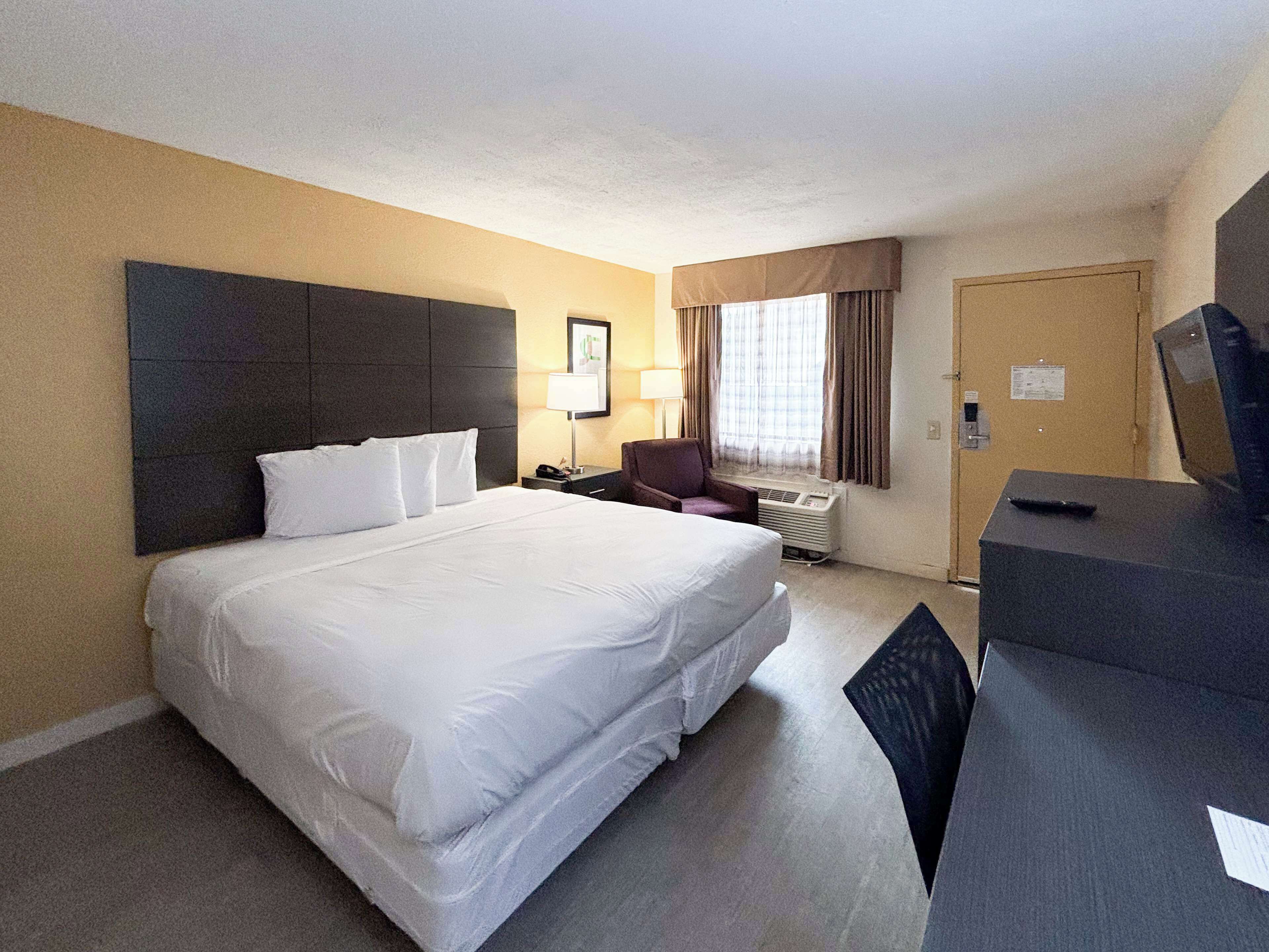 A hotel room with a large bed, a desk, a chair, a TV, and a window with curtains.