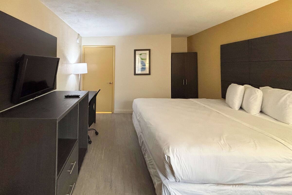 A hotel room with a bed, a desk with a TV, a wardrobe, and a door.