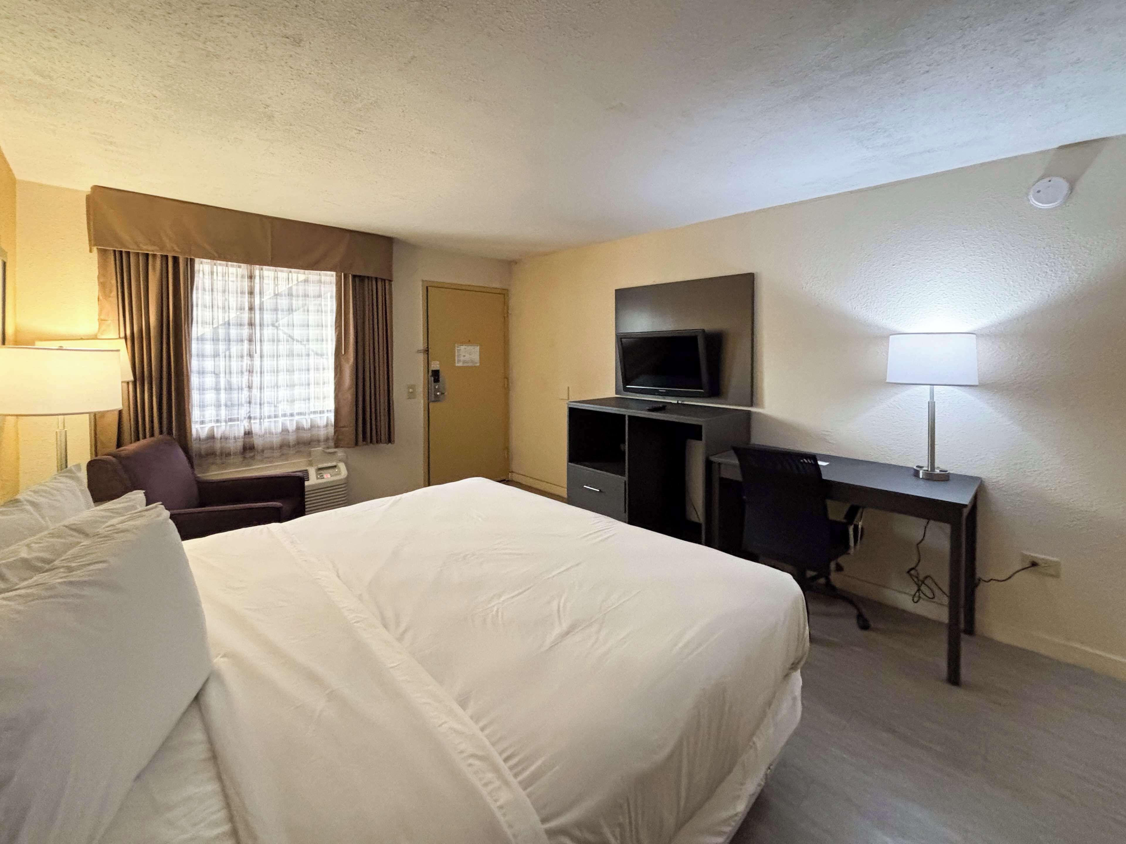 A hotel room with a large bed, a desk with a computer, a television, and a window with curtains.