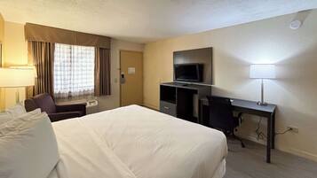 A hotel room with a large bed, a desk with a computer, a television, and a window with curtains.