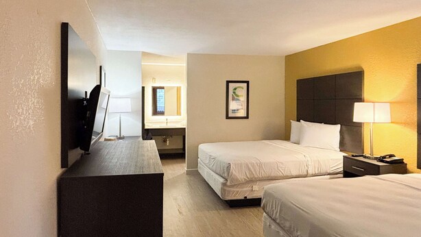 A hotel room with two beds, a desk, a TV, a bathroom, and a framed picture on the wall. - Motel 6 Charlotte, NC - Northlake (Charlotte)