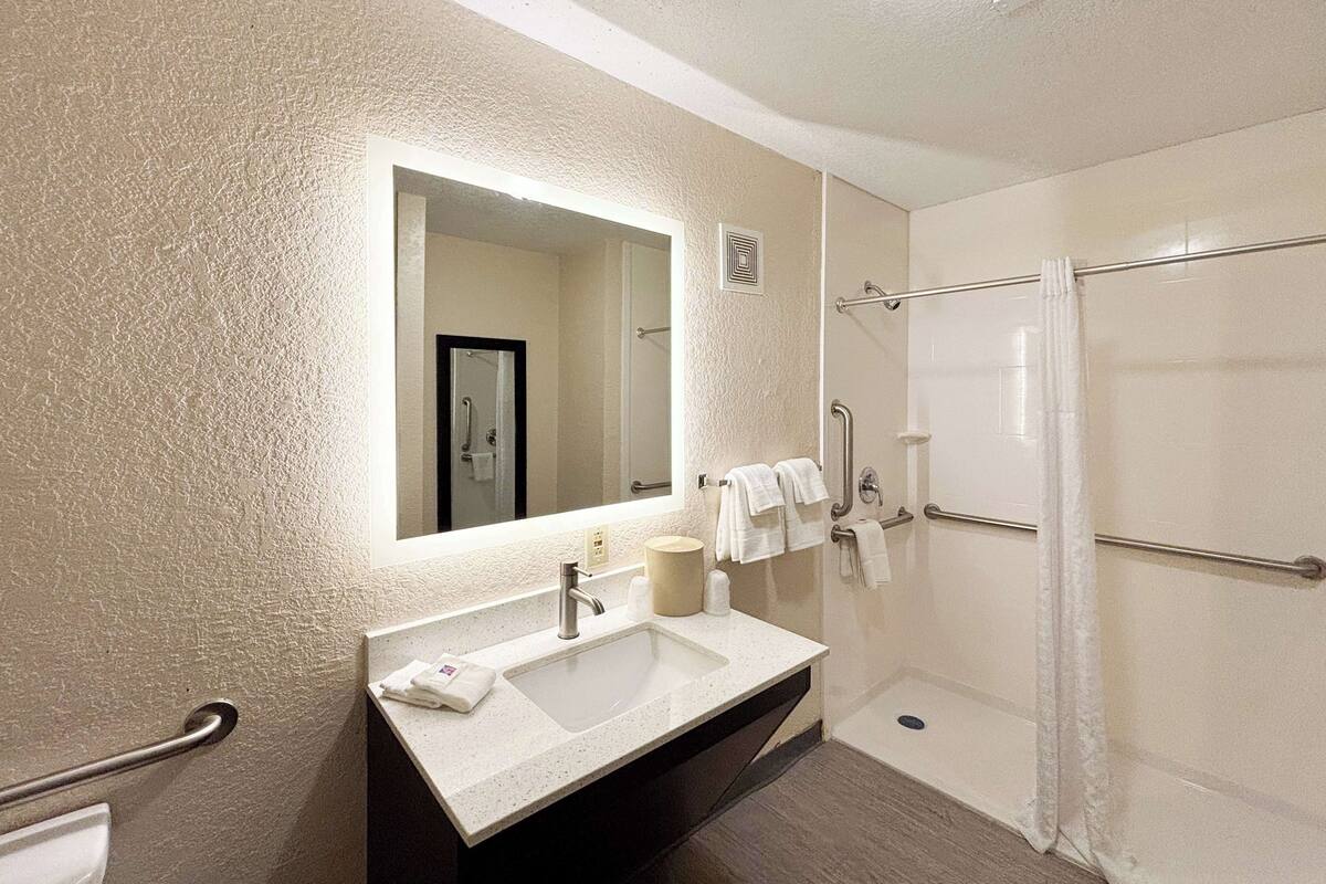 A bathroom with a sink, mirror, and shower.