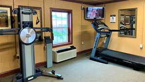 A gym with cardio equipment, a treadmill, and a mirrored wall.