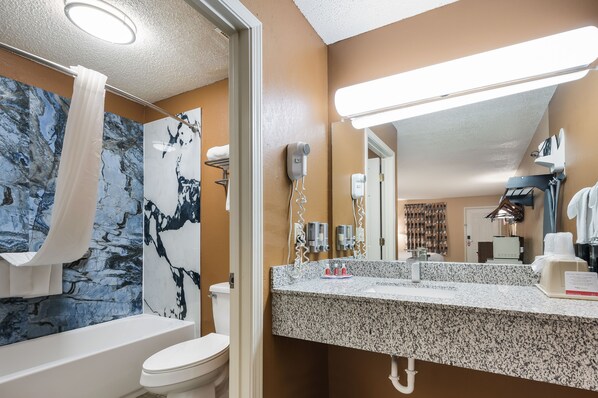 A bathroom with a marble wall, a white bathtub, a sink with a granite countertop, and a mirror.