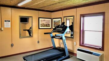 A fitness center with a treadmill, mirrors, framed pictures, and an air conditioning unit.
