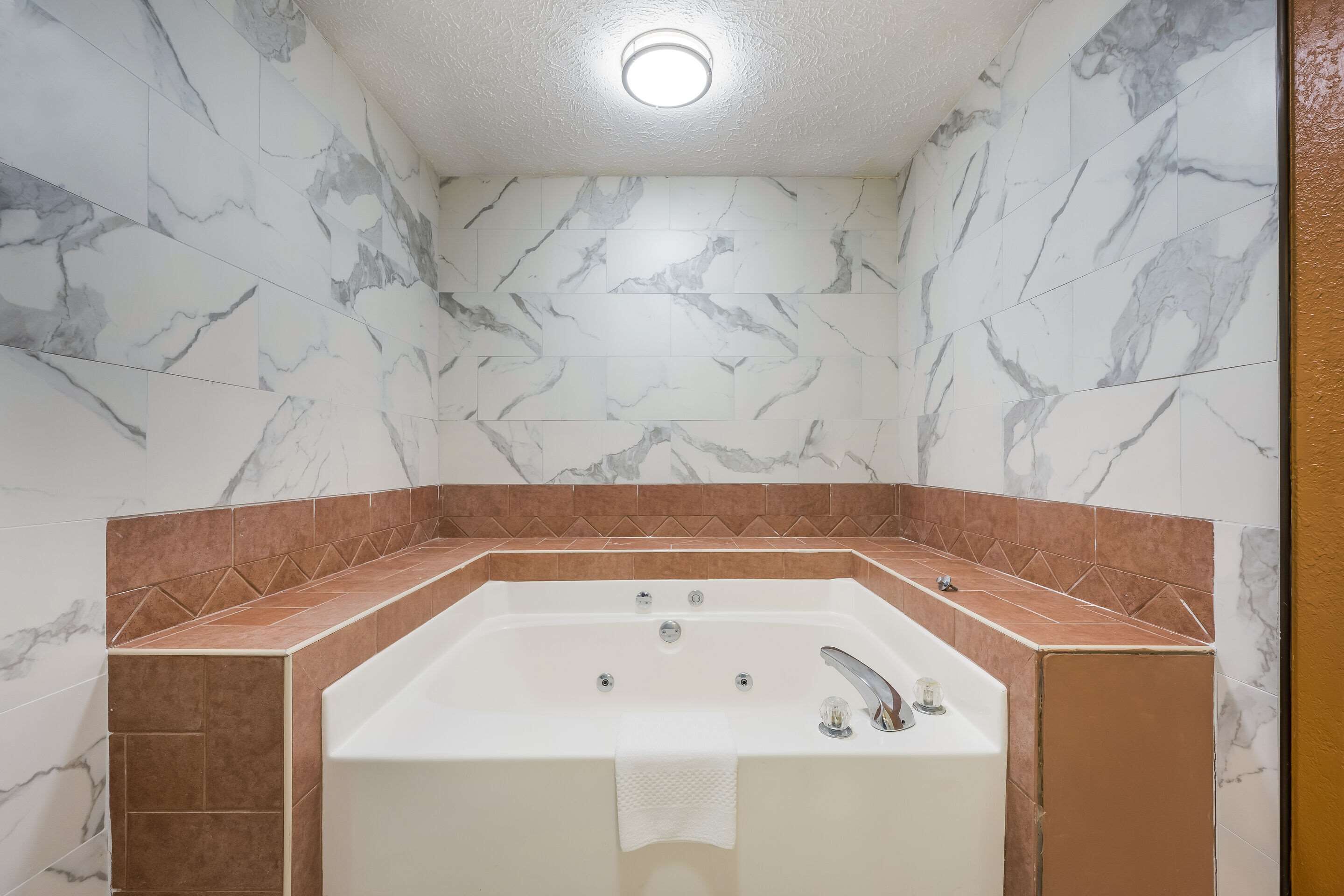 Un baño con pared de mármol y bañera con detalle de azulejos marrones.