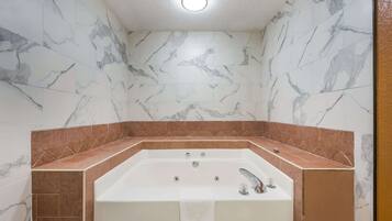 Un baño con pared de mármol y bañera con detalle de azulejos marrones.
