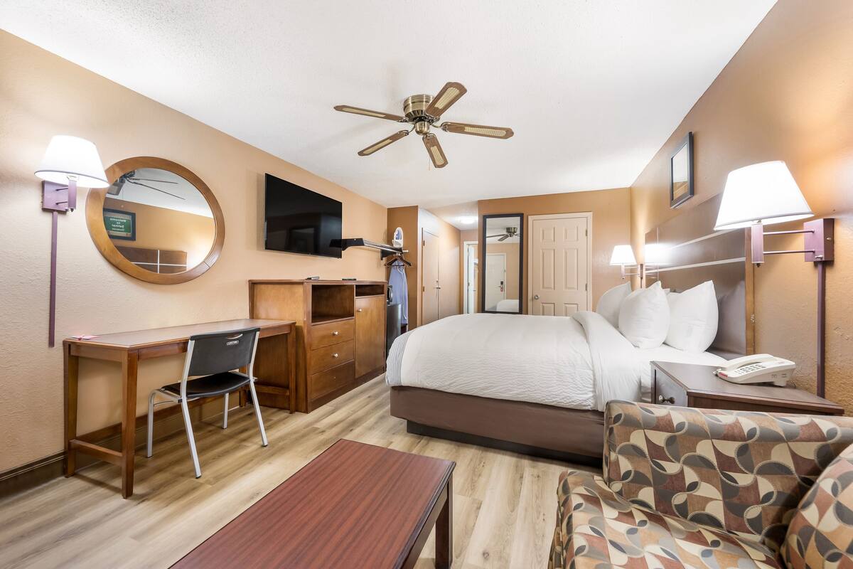 Una habitación de hotel con cama, escritorio, silla y ventilador de techo.