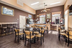 Un comedor con varias mesas y sillas, una estación de café y una zona de cocina.