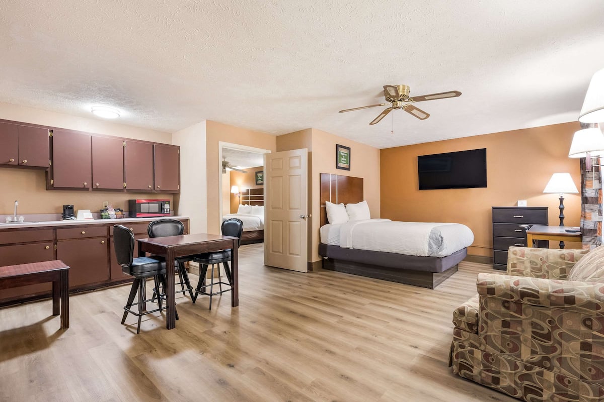 Habitación de hotel compacta con kitchenette, una cama, un escritorio con dos sillas y un sillón estampado.