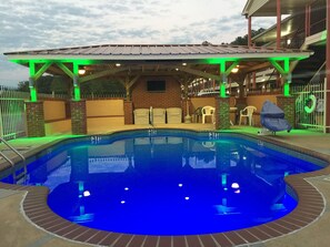 Una piscina con zona cubierta, pared de ladrillo y entrada con reja.