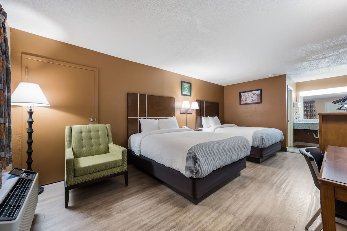 Habitación de hotel con dos camas, una silla, un escritorio, una lámpara y un espejo.