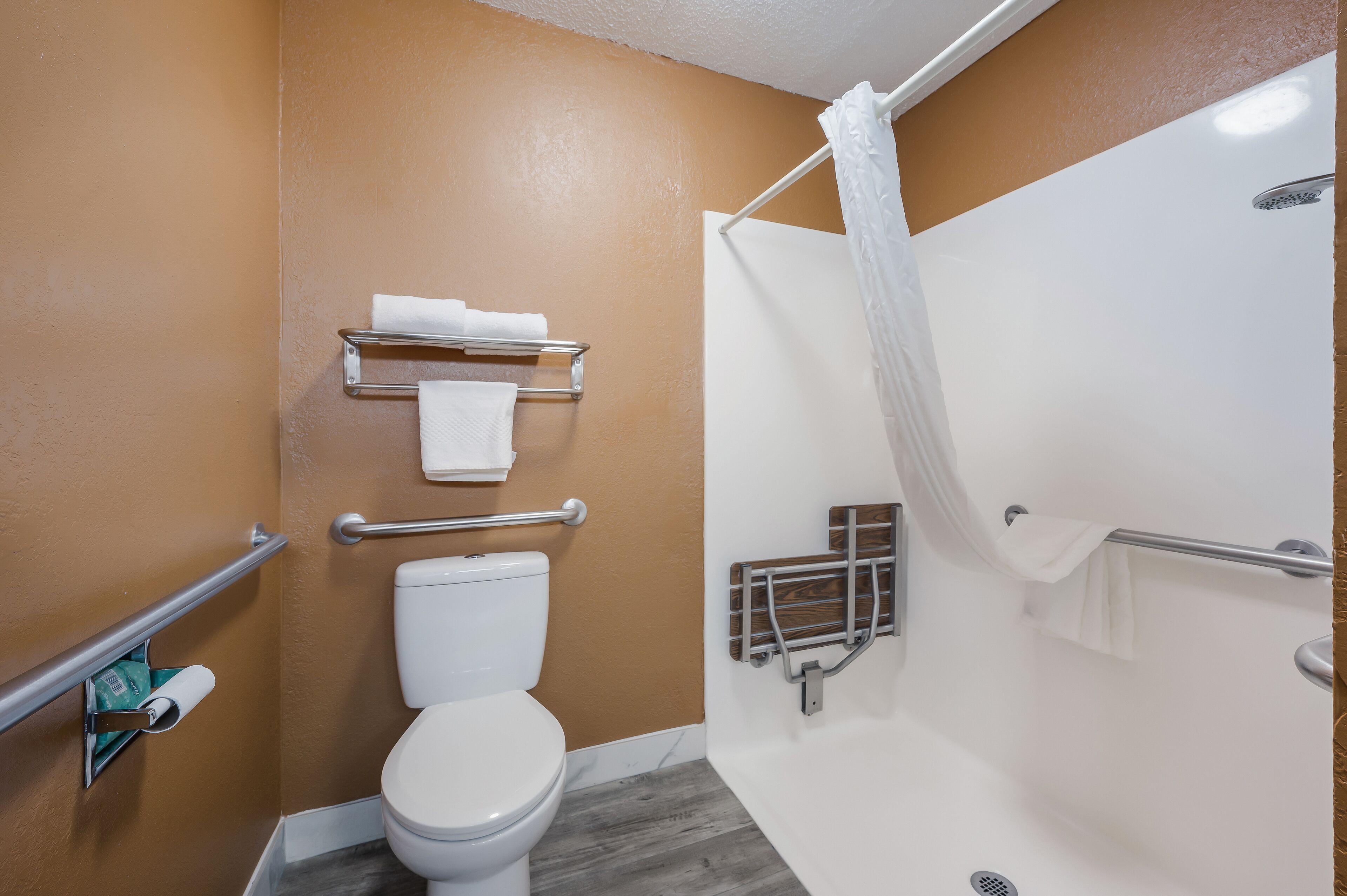 A bathroom with a white toilet, a shower with a white curtain, and a towel rack with two towels.
