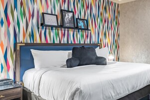 Habitación de hotel con cama, mesita de noche, pared con patrones geométricos de colores y cuadros enmarcados.