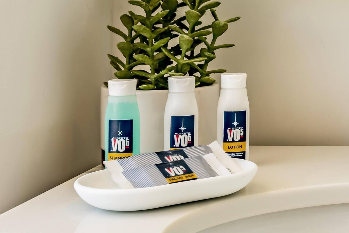 A bathroom with a white sink, a plant, and three bottles of facial bar lotion.
