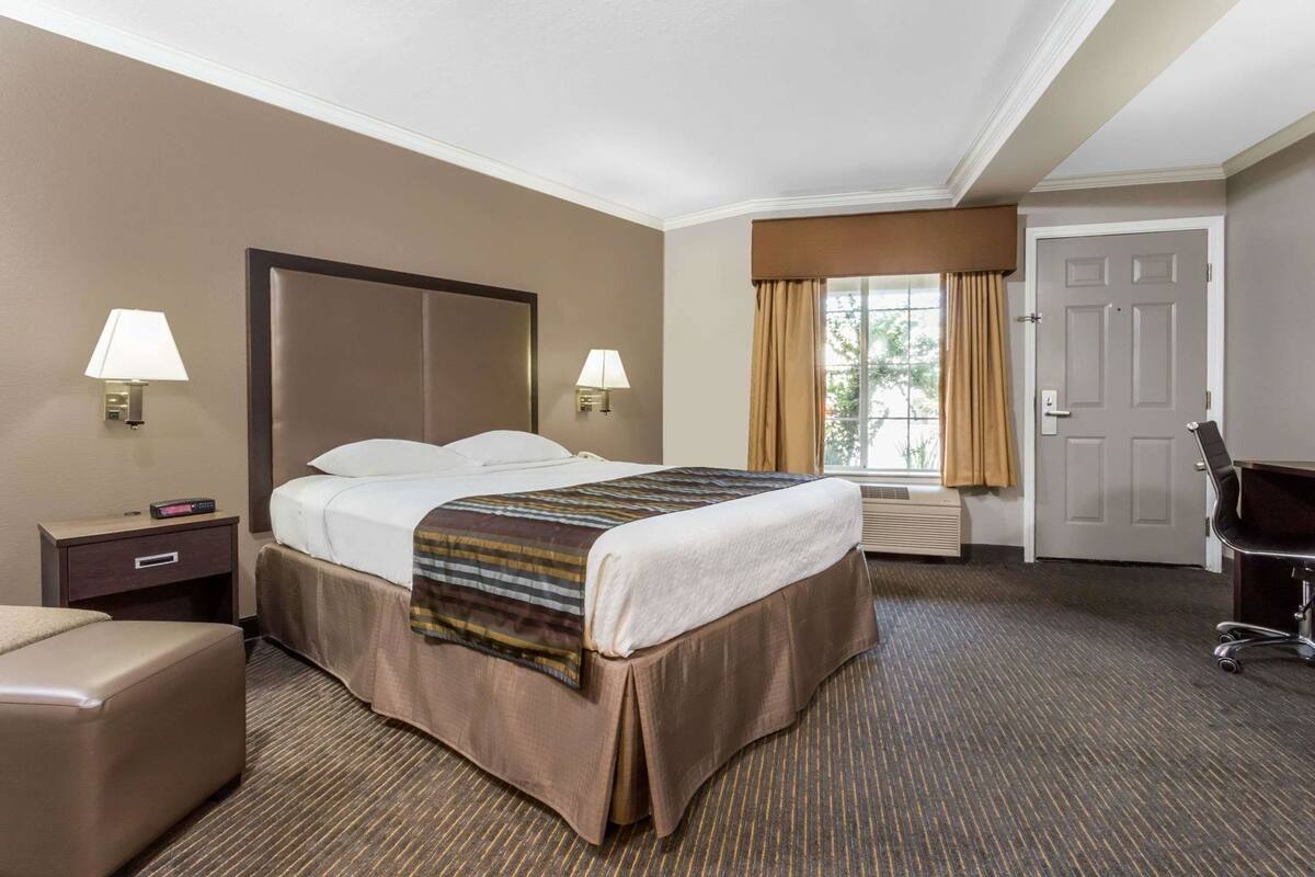 A hotel room with a large bed, two bedside lamps, a desk with a chair, and a door.