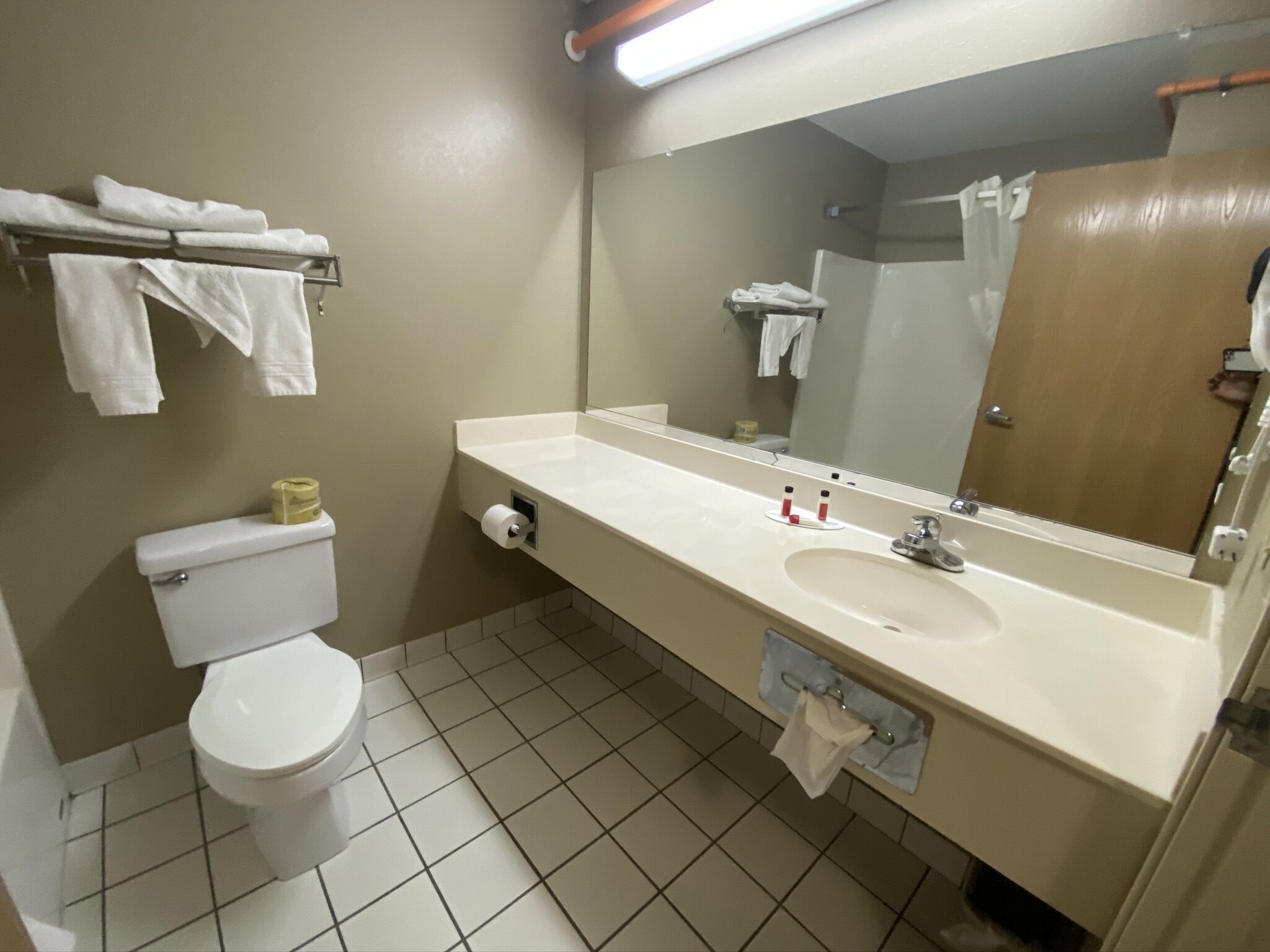 Un baño de hotel estándar con inodoro, lavamanos y espejo.