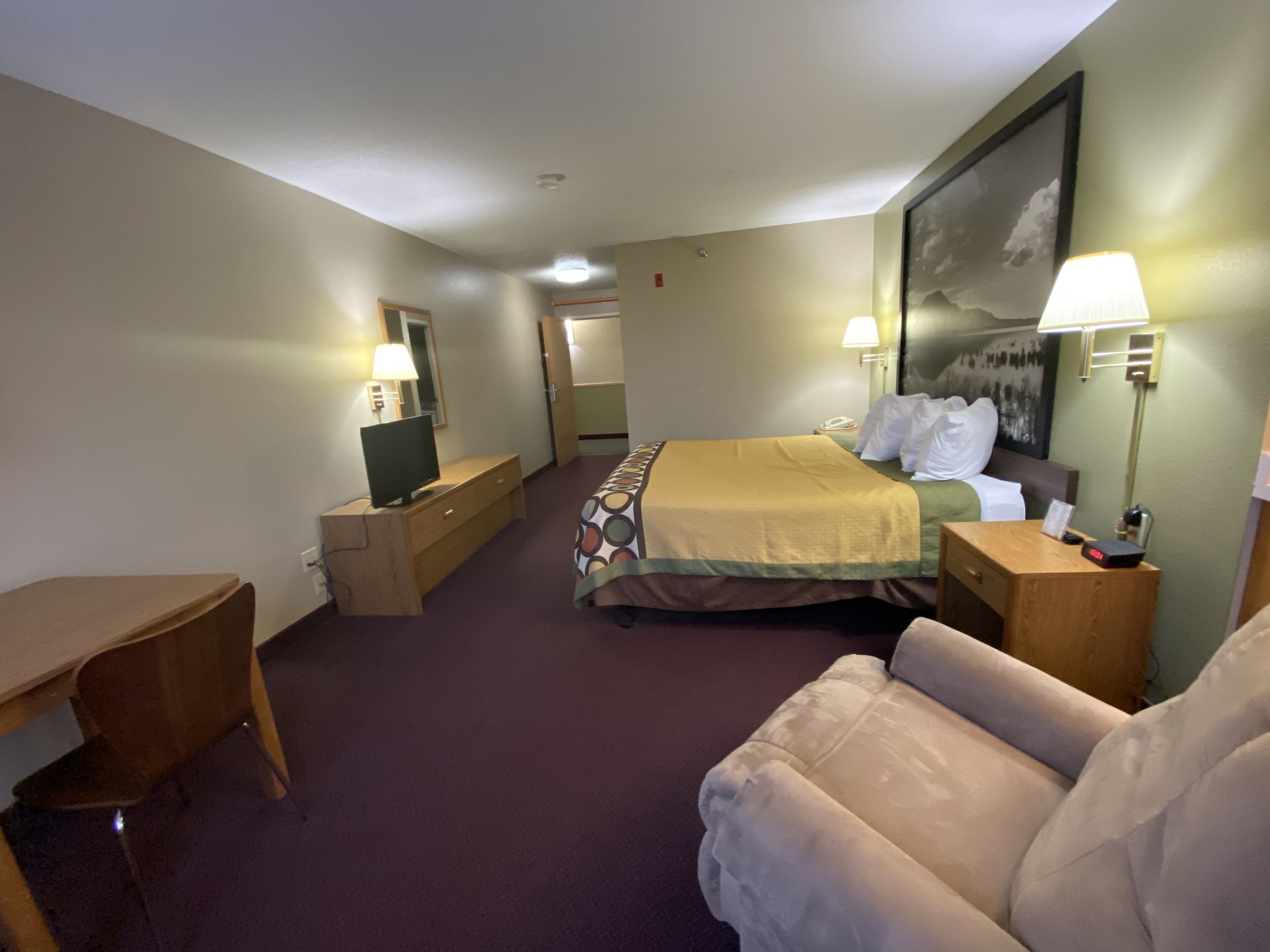 A hotel room with a bed, a desk, a chair, a TV, and a lamp.