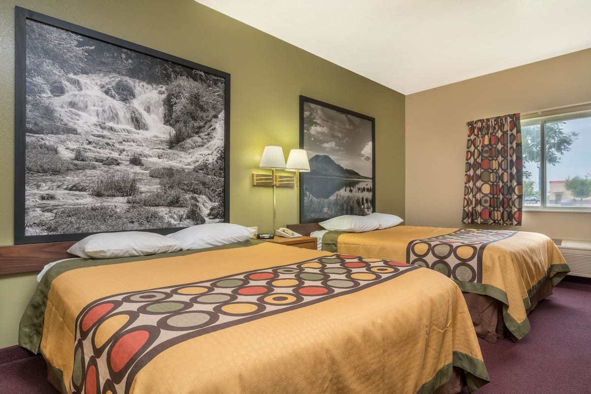Ein Hotelzimmer mit zwei Betten, einem großen gerahmten Gemälde einer Wasserfalllandschaft, einer Lampe und einem Fenster mit Vorhängen.