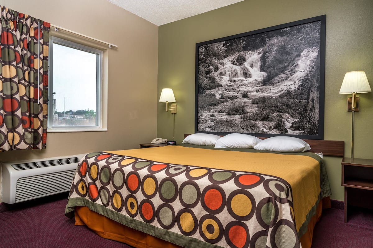 Ein Hotelzimmer mit einem Bett, einem großen Wandbild eines Wasserfalls, zwei Nachttischlampen, einem Heizgerät und einem fenster mit Vorhängen.