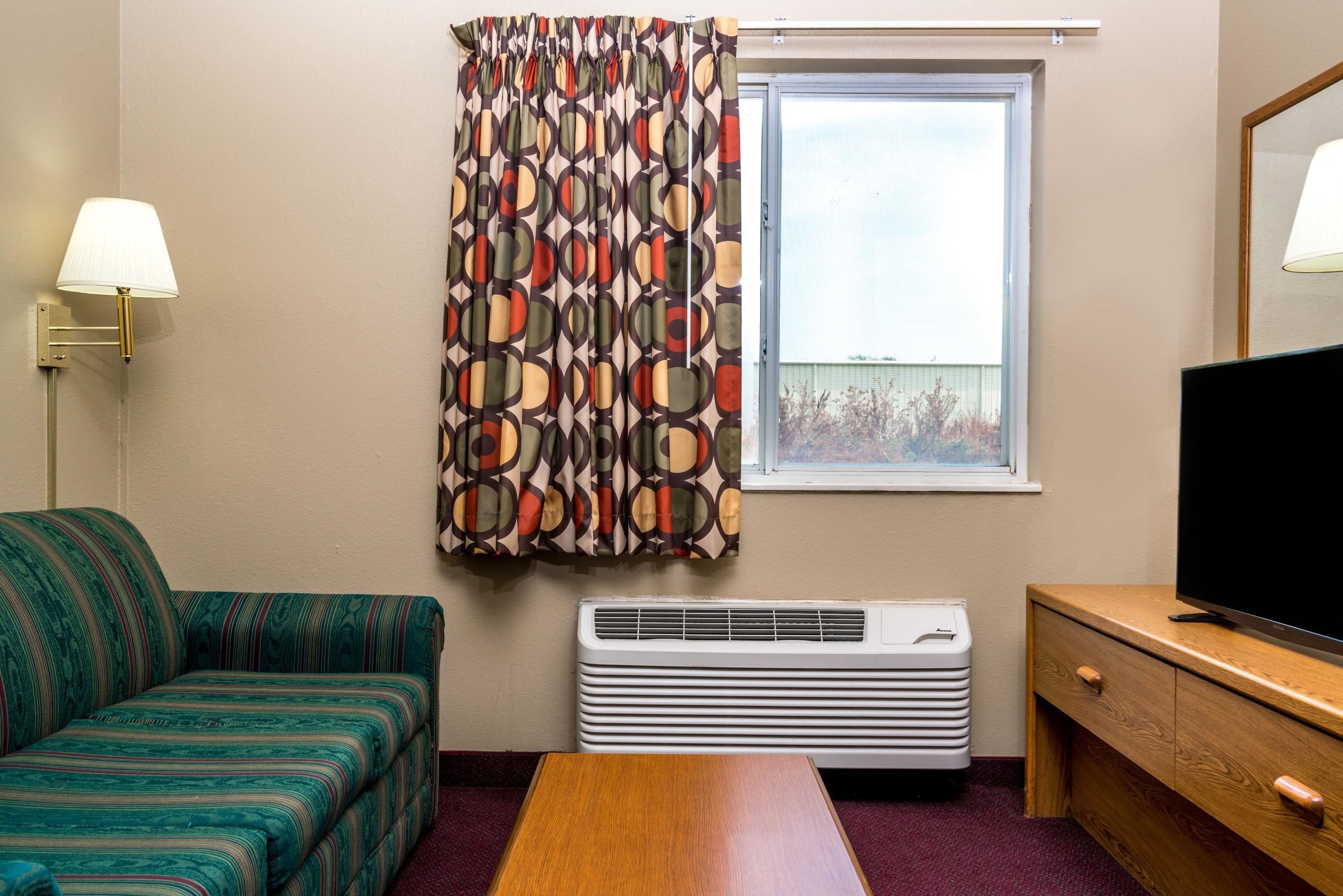 A room with a sofa, a table, a TV, a heater, and a window with curtains.