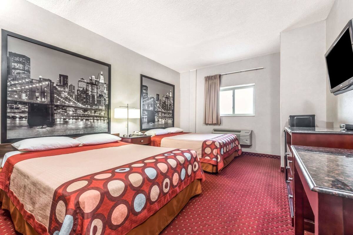 A hotel room with two beds, a TV, a desk, and a window with curtains.