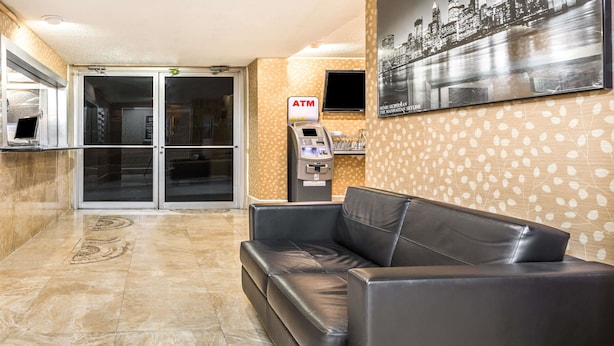 A lobby with a reception desk, an ATM, a sofa, and a cityscape mural. - Super 8 by Wyndham North Bergen NJ/NYC Area (North Bergen)