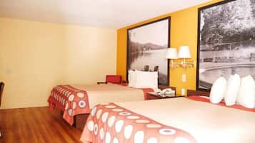 A hotel room with two beds, a wooden floor, a red chair, a nightstand with a lamp, and a large framed picture of a lake.