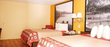 Habitación de hotel con dos camas, suelo de madera, una silla roja, una mesita de noche con lámpara y un cuadro grande con un paisaje de un lago.