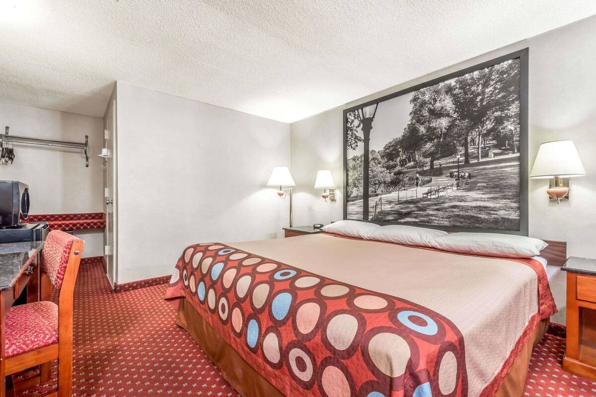 A hotel room with a bed, a desk, two lamps, and a large black and white photograph on the wall.