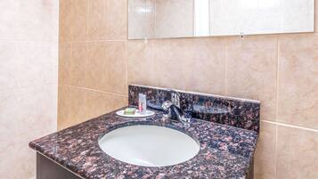 A bathroom with a granite countertop sink, a mirror, and beige tiled walls.