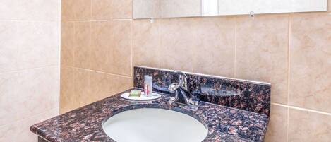 A bathroom with a granite countertop sink, a mirror, and beige tiled walls.