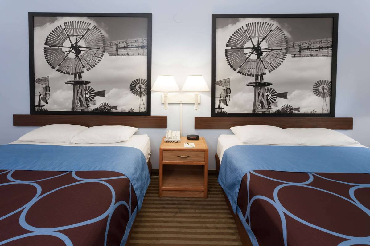 A hotel room with two beds, a nightstand with a lamp, and two framed windmill pictures on the wall.