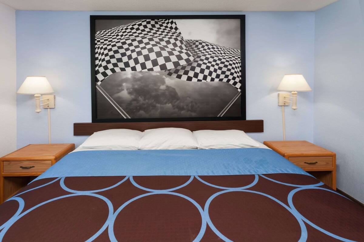 A hotel room with a bed, two bedside tables, a wall-mounted artwork, and two wall-mounted lamps.