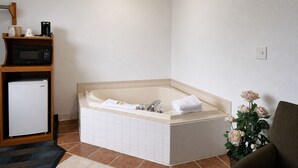 A bathroom with a bathtub, a microwave, a refrigerator, a sink, and a potted plant.