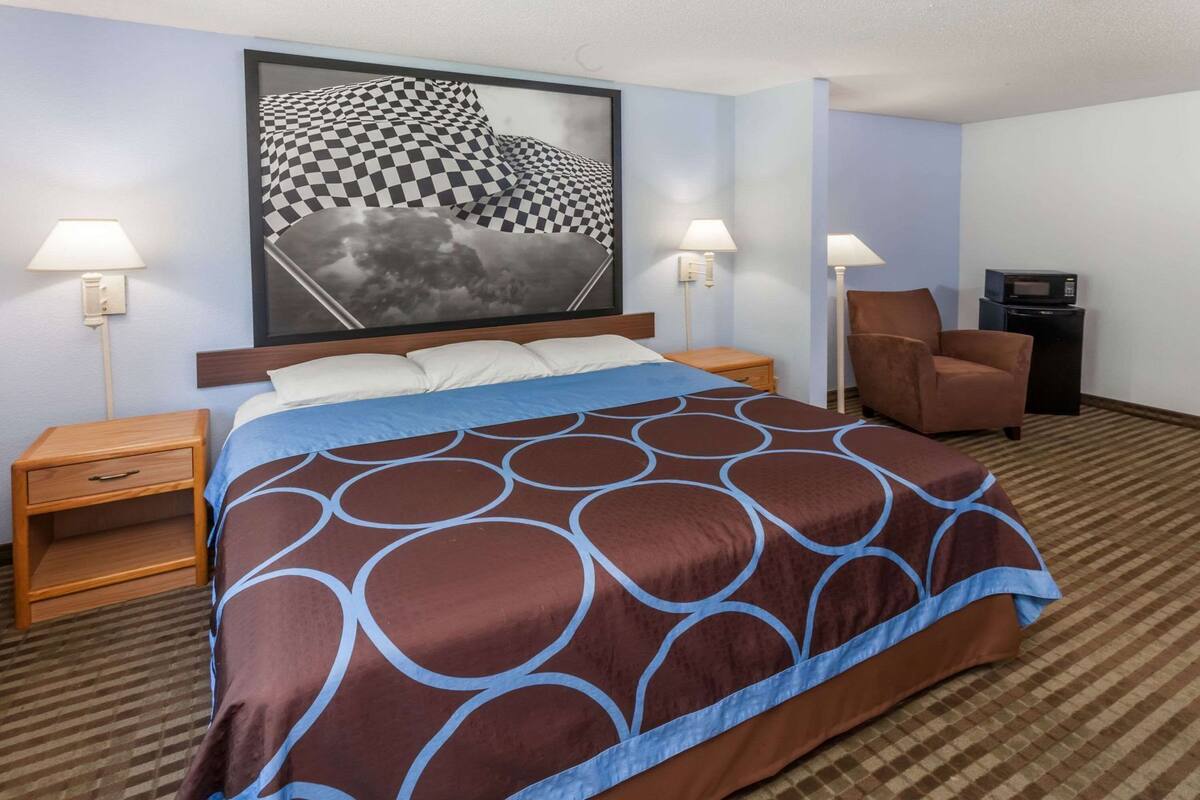 A hotel room with a large bed, two bedside tables, a chair, a television, and a framed picture on the wall.