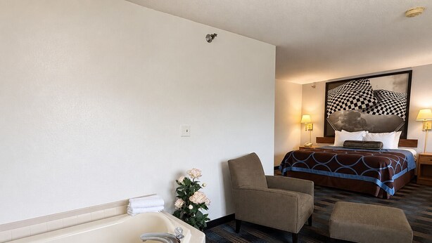 A hotel room with a bathtub, a bed with a checkered headboard, a chair, and a small table.