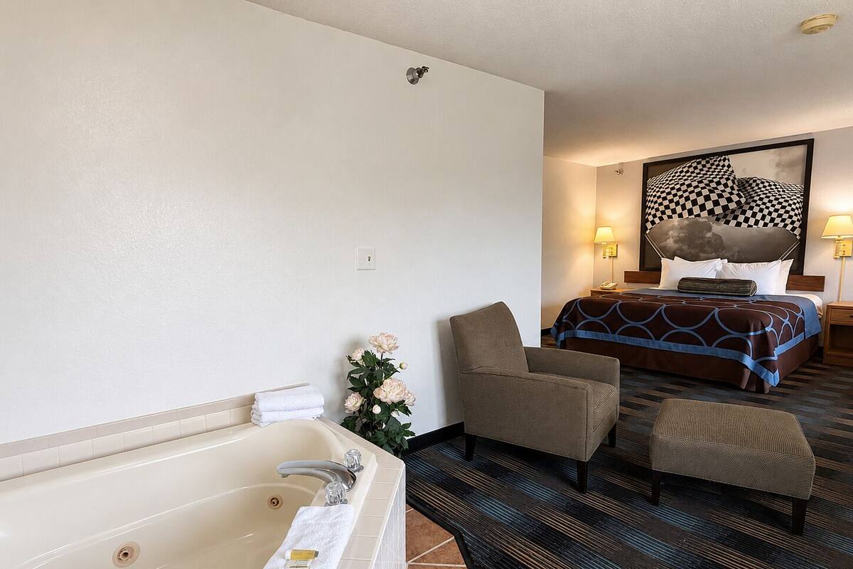 A hotel room with a bathtub, a bed with a checkered headboard, a chair, and a small table.
