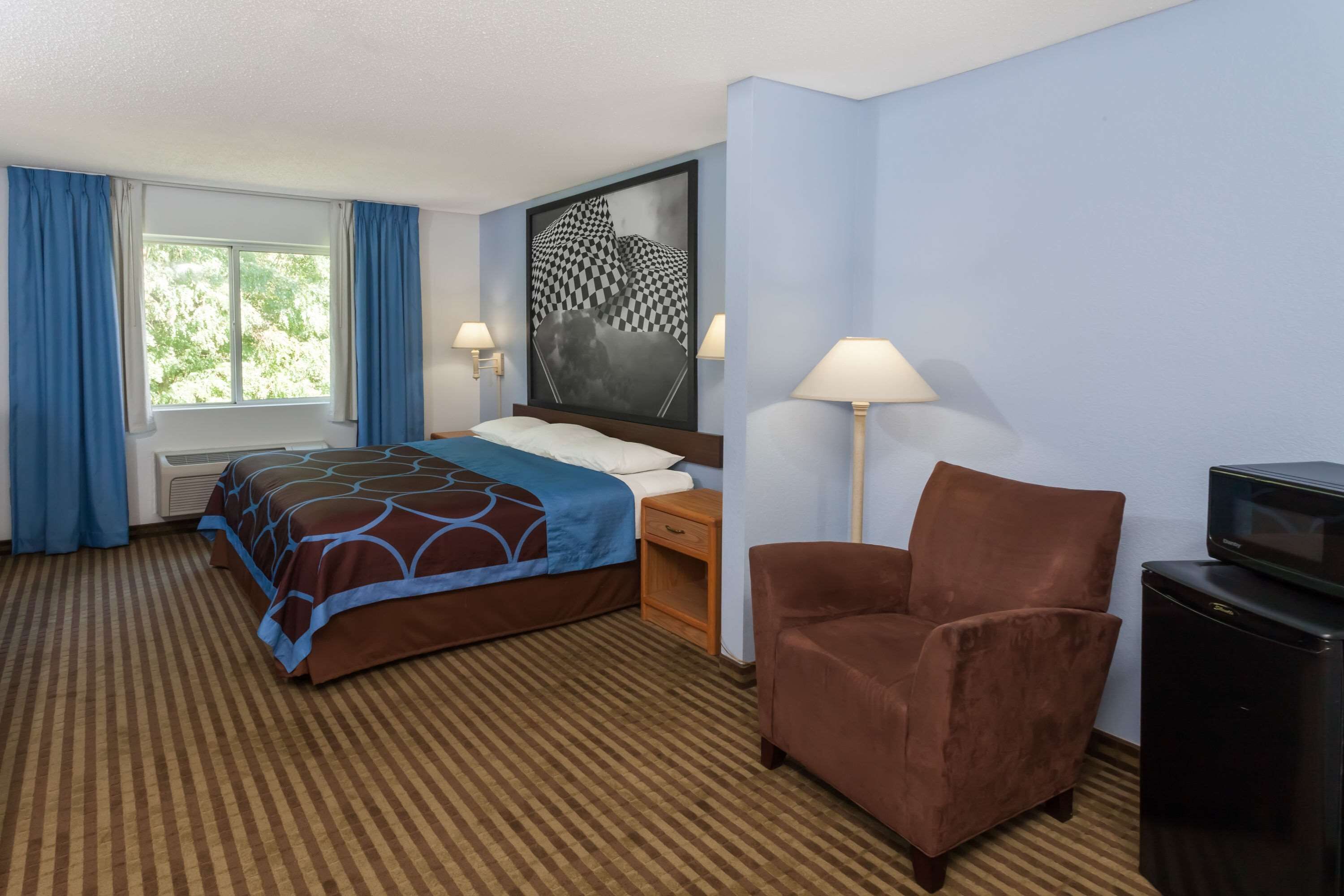 A hotel room with a bed, a chair, a TV, and a large window with curtains.