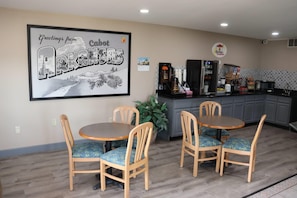 A dining area with two round tables and four chairs, a kitchen area with appliances, and a framed welcome sign on the wall. - Super 8 by Wyndham Cabot (Cabot)