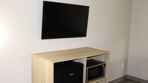 A room with a flat-screen TV mounted on the wall, a wooden cabinet with a microwave inside, and a black appliance below the cabinet. - Super 8 by Wyndham Cabot (Cabot)